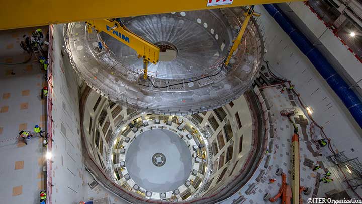 The first major machine component - the cryostat base weighing 1,350 tonnes - is lifted by a overhead crane and lowered into the Tokamak assembly pit.